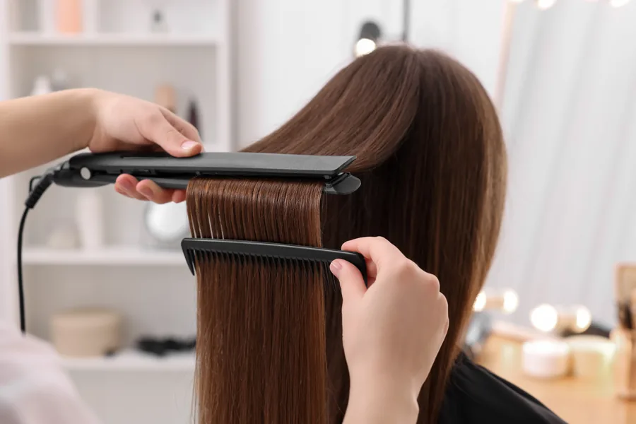 Thợ tóc ép thẳng mái tóc dài của khách bằng máy ép và lược