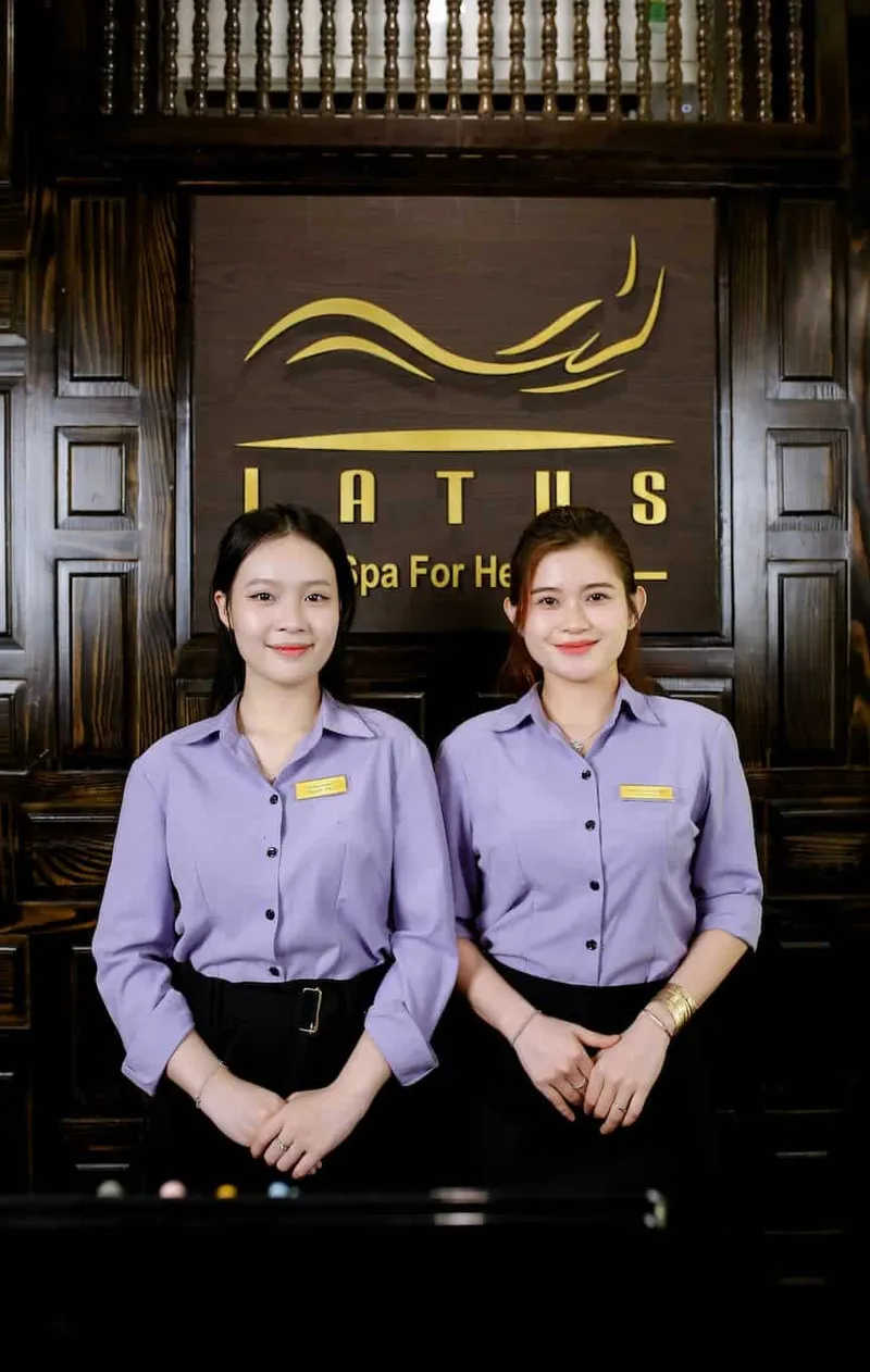 Hai lễ tân Latus Spa mặc đồng phục tím đứng trước bảng hiệu Latus Spa For Health